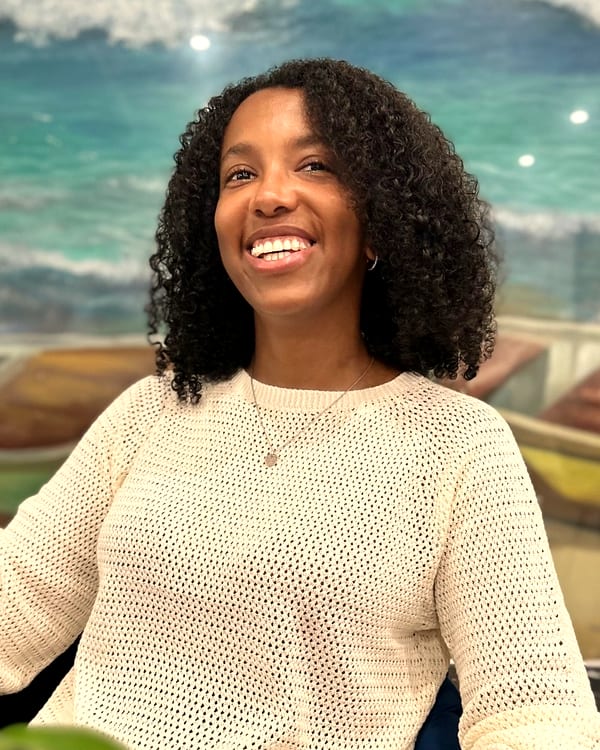 Jainaba Sey laughing warmly, wearing a cream knit sweater